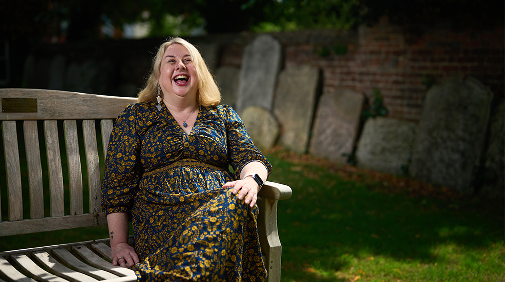 Nat Doig sitting on a bench in a graveyard and laughing
